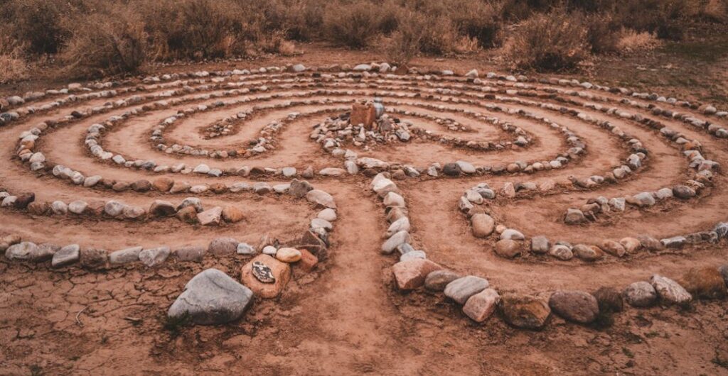 A stone labyrinth with a person sitting in the center in a desert landscape.