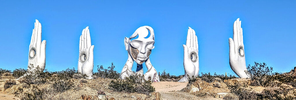 A large surreal sculpture of a face and a hand against a blue sky.